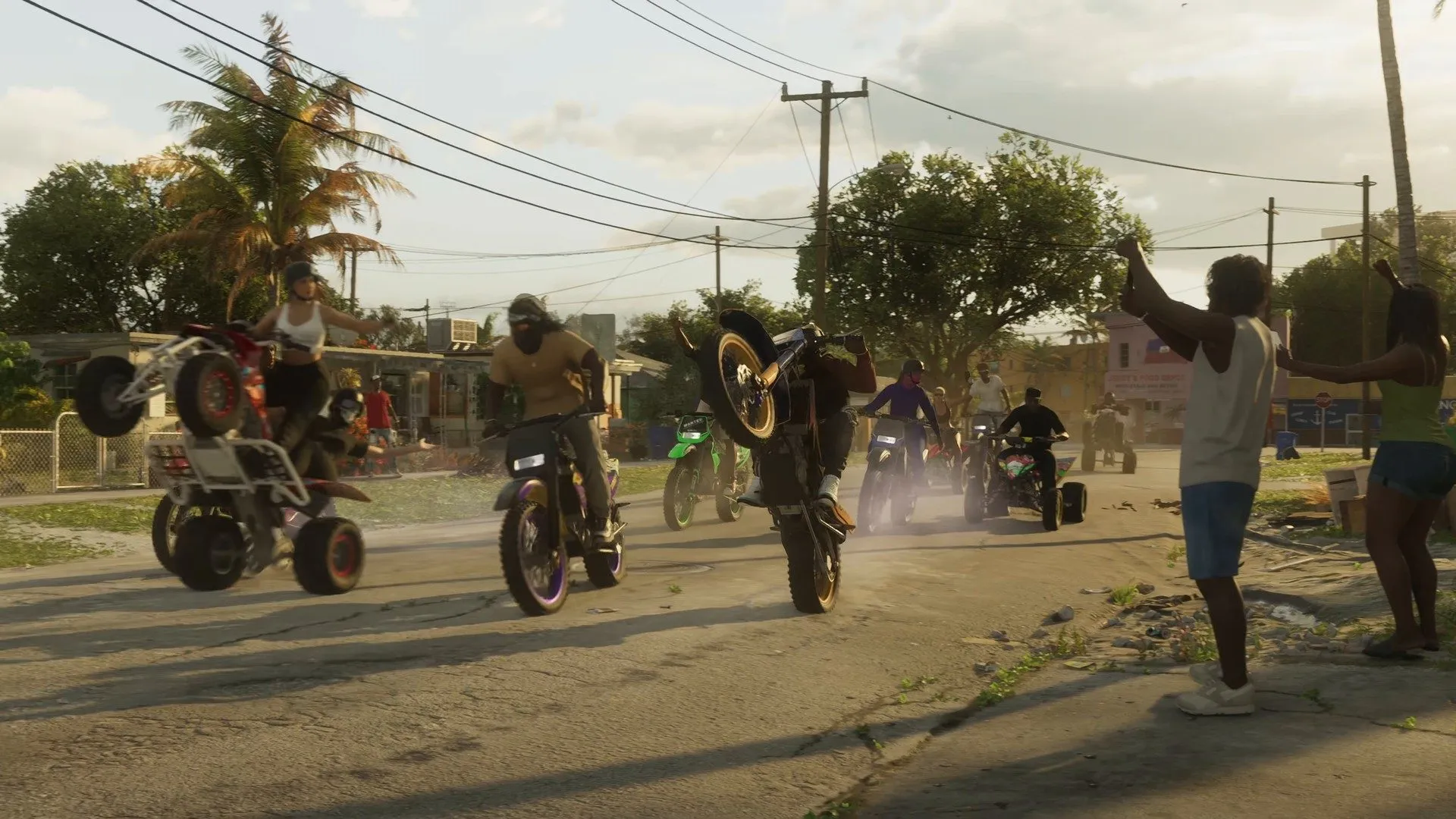 Riders pop wheelies on dirt bikes and quads on a dusty street