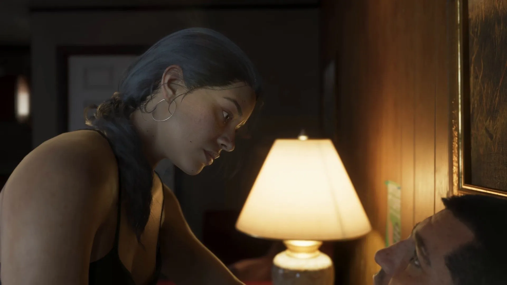 Lucia, her hair in a braid, leans over a shirtless man lying beside a table lamp