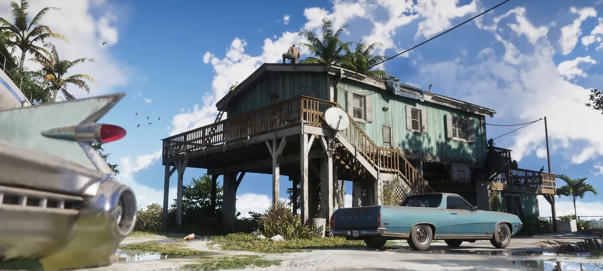 A pale-blue low pickup parked in front of a teal stilt house