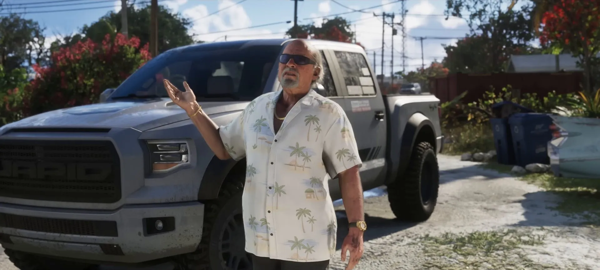 Brian Heder, an older man in a palm-print shirt and sunglasses, gestures beside a grey pickup