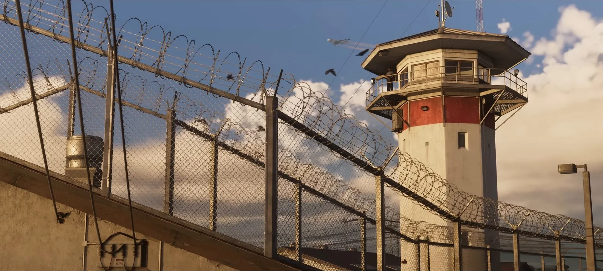 Prison watchtower behind a razor-wire fence under a blue sky